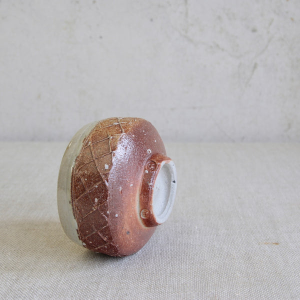 Top down shot showing a Phil Rogers stoneware pottery chawan stoop on its side. The British ceramic art piece showcases a reddish clay body, salt glaze, and thick nuka interior finish.