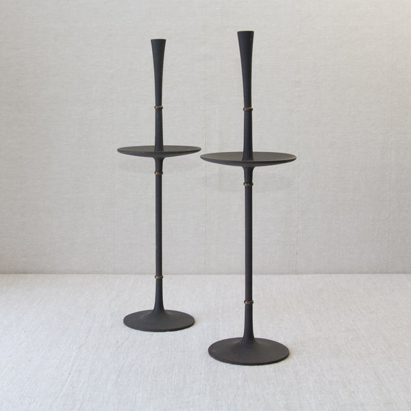 Lead image of a pair of minimalist Scandinavian candlesticks or candle holders, designed by Jens Quistgaard. The materials include cast iron which is matt black, and brass which is nicely patinated.