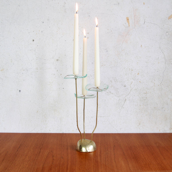 Rare handmade Swedish candlestick in brass and glass, mid-century floral form. The candelabra holds three white dinner candles that are lit.