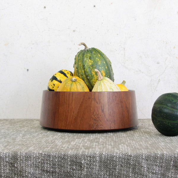 Wooden bowl with gourds on a textured surface. Large staved teak fruit bowl by Jens Quistgaard for Dansk Designs. Handmade in Denmark, a mid-century icon of Scandinavian modern design.