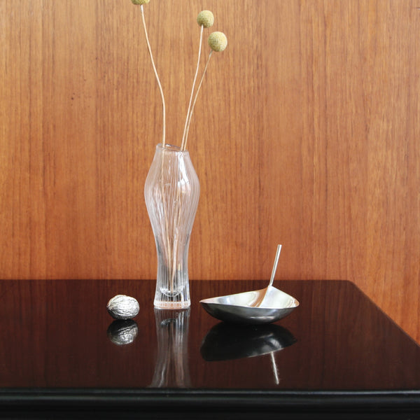 Artistic mood shot still life showing a Kantereli glass vase with dried plants on a reflective black surface against a wooden background. The Modernist leaf-shaped silver bon bon dish is by Tapio Wirkkala, Finnish design, for sale in UK.