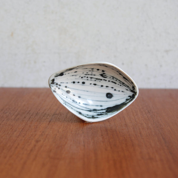 Ceramic dish with black speckles on a wooden surface. Elegant biomorphic shallow dish by Susan Parkinson, abstract stripe design, made in Richard & Susan's short lived Brabourne Lees pottery in Kent.
