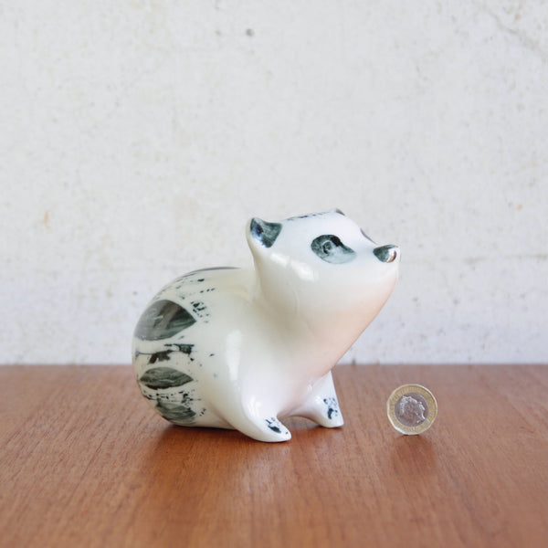 Mood shot showing a postwar studio pottery bear sculpture, hand-decorated porcelain by Susan Parkinson. The figure stands next to a one pound coin for scale.