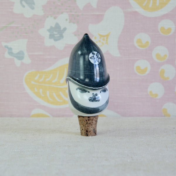A ceramic figurine of a policeman's head wearing a pointed black helmet, mounted on a cork stopper. Susan Parkinson's design was originally created in response to American demand for distinctly British Parkinson Pottery designs.
