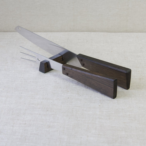 Top-down view of a carving set in stainless steel and black oak, designed by Tapio Wirkkala for Hackman, Finland. The fork and knife are laying in their block stand.