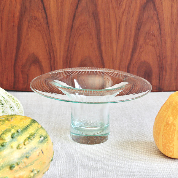 Artistic still life showing a Nordic modern glass art bowl by Helena Tynell stood amongst three pumpkins.