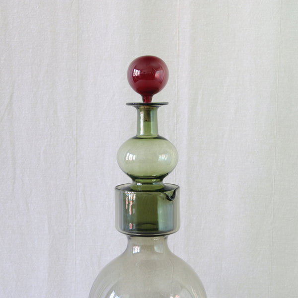 A rare vintage 1957 Kaj Franck Kremlin Kellot juice set, comprising a smoke-grey water pitcher and bottle-green decanter crowned by a ruby-red stopper. For sale in the UK.