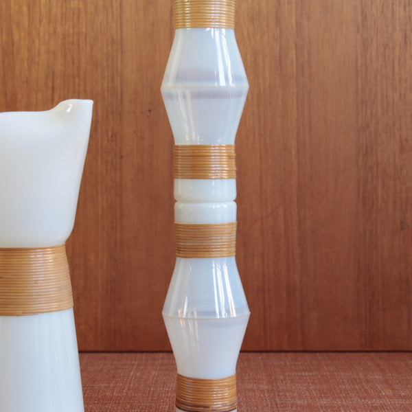 Close up of a vintage white Opaline carafe and glasses with applied rattan, representing the functionalist Scandinavian aesthetic central to mid-century Danish design.