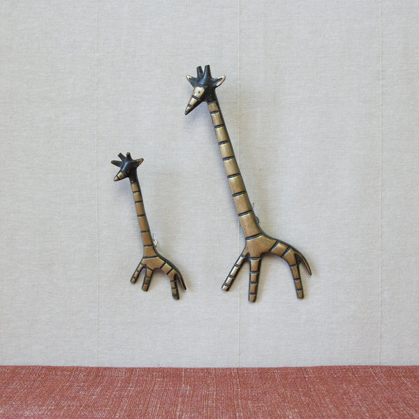 Far away shot showing two black and gold brass giraffe animals hanging on a wall. This pair of MidCentury Modern wall hangings were designed by Walter Bosse. 