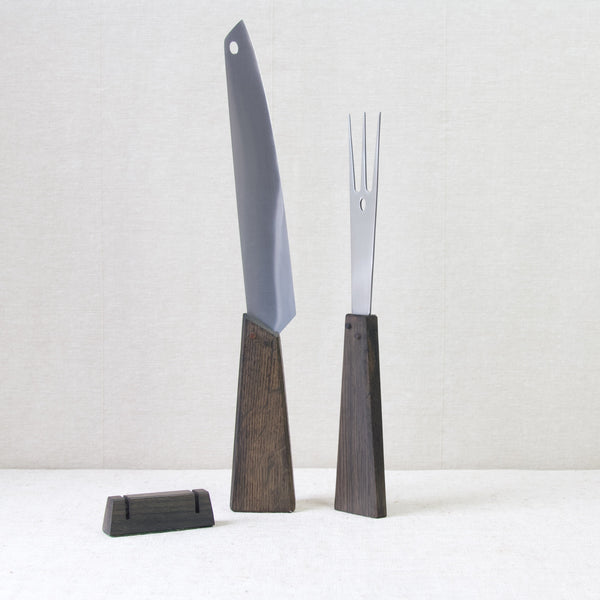 Stylish mood image showing a carving knife and a carving fork stood up straight pointing at the ceiling. The little block stand is stood to the left. This design is by Tapio Wirkkala, many of his MidCentury Scandinavian designs can be found at London design gallery Art & Utility, who offer worldwide shipping.