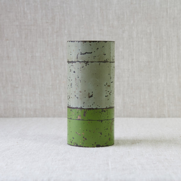 A tall grey coloured storage jar stood atop a smaller example in green. Both canisters are formed from brass and were probably made in Britain or Germany in the 1920s or 1930s.
