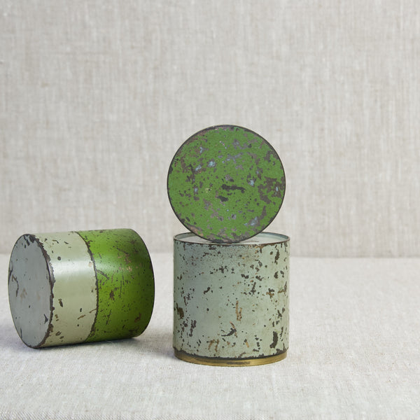 Stylised mood image showing a variety of cylindrical tins laying on an off white linen cloth.
