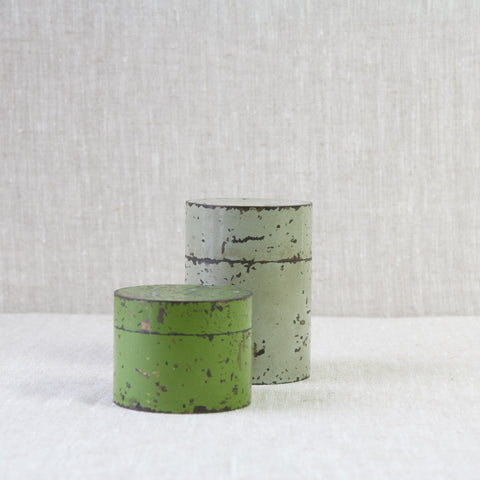 Two colourfully enamelled tins, one green one grey. Made by the same manufacturer in the early twentieth century.