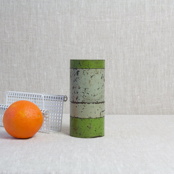 Two cylindrical storage tins similar to the work of Hans Przyrembel. The tall jars in grey and green stand next to a white letter rack by Mathieu Matégot and an orange fruit.