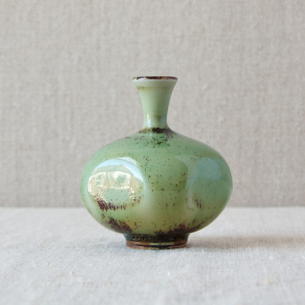 A small vase handmade by Friberg in 1972. This piece is beautifully glazed with an aqueous turquoise-green, and features bold speckles of deep oxblood red inclusions.
